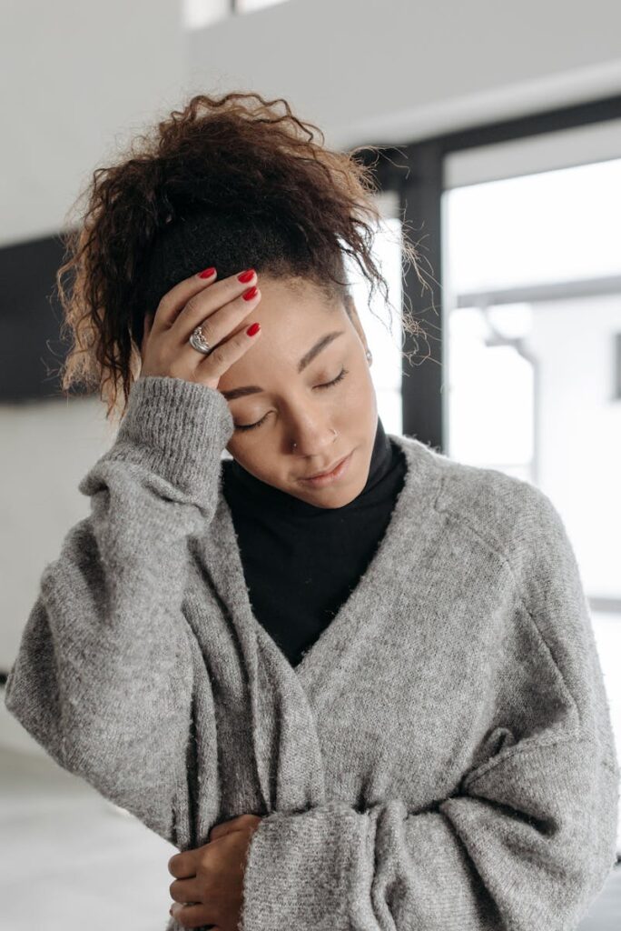 A young woman with a headache and malaise, wearing a cozy sweater indoors.